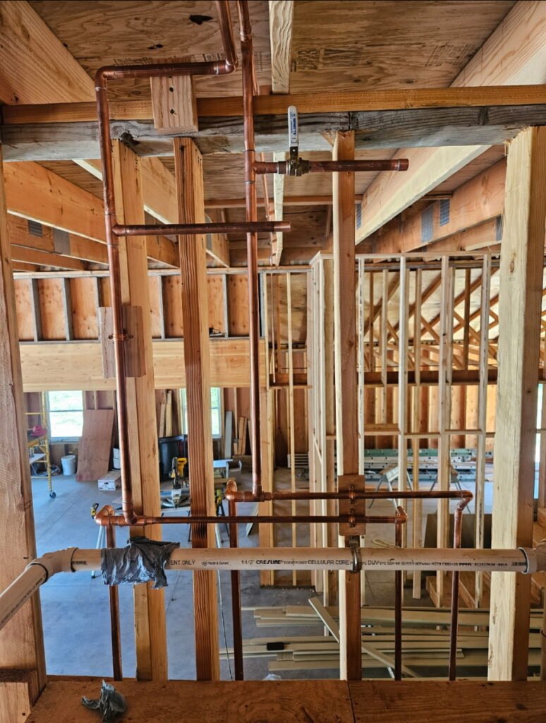 New construction plumbing rough-in with copper water lines installed through exposed wood framing, showing clean pipe layout and organized jobsite inside a residential build in progress