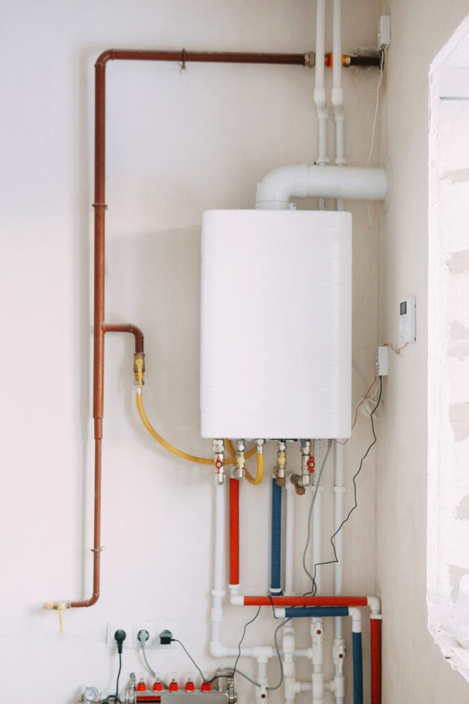 Wall-mounted tankless water heater installed on a clean interior wall, with exposed plumbing lines, shutoff valves, and vent piping visible, showing a compact on-demand hot water system setup.